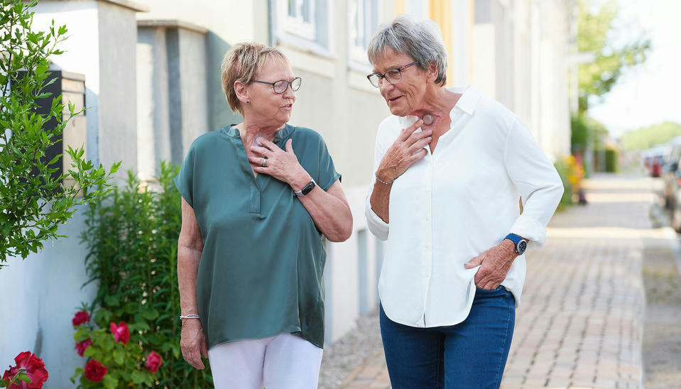 Two women with a neck stoma walking on the street using provox life hme while talking.