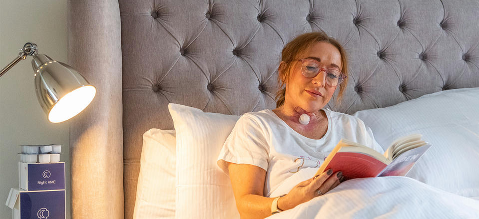 atos-medical-clinical-evidence-ward-study woman with stoma wearing Atos night time HME reading in bed before sleep, with boxes of Night HME product beside bed